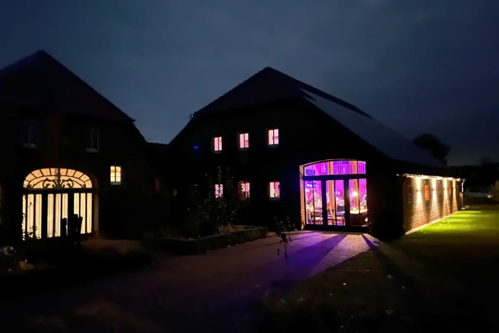 Dunkles Gebäude bei Nacht mit beleuchteten Fenstern und großem Eingang, innen pink-violettes Licht, davor Einfahrt