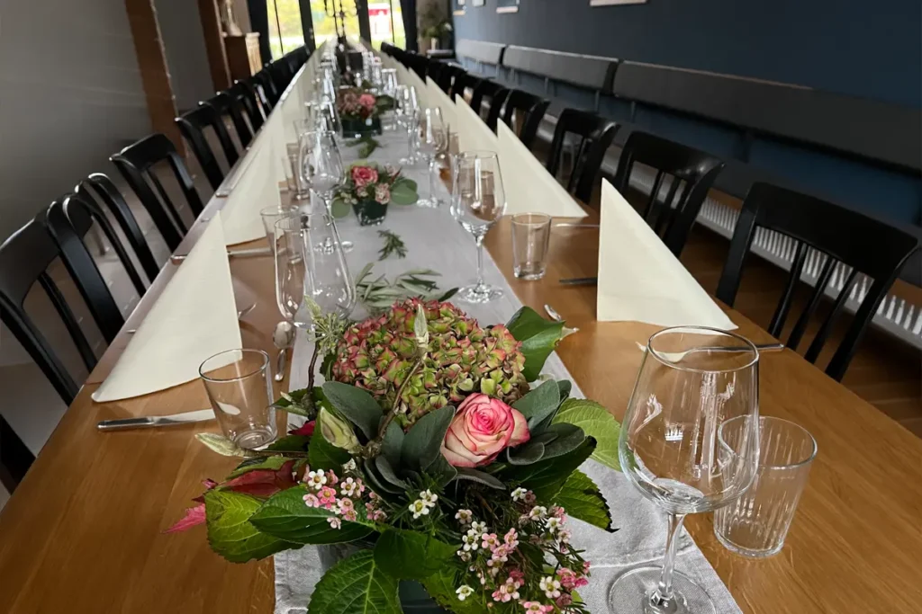 Langer gedeckter Tisch mit weißen Servietten, Gläsern und Blumenarrangements als Tischdekoration in einem Restaurant